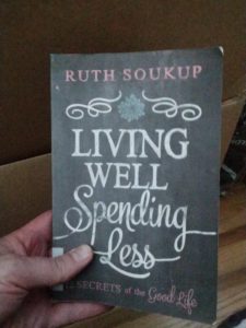 My hand holding a copy of Living Well, Spending Less by Ruth Soukup.